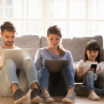 Family with kid sitting on floor at home using devices