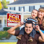 Happy Mixed Race Young Family in Front of Sold Home For Sale Real Estate Sign and House.