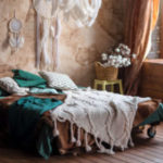 Stylish room interior with large comfortable bed. Beige and white dream catchers and feathers hanging above gypsy or hippie slyle bed in dark autumn bedroom interior