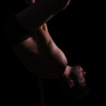 Dramatic dark portrait of a young man pole dancing. Dark background studio shot.