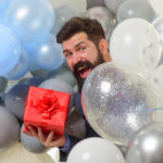 Festive event or birthday party. Happy birthday guy holds helium balloons and gift box. Handsome man celebrating something. Bearded man in suit holds birthday gift. People, joy, birthday, celebration.