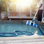 Man cleaning swimming pool with vacuum tube cleaner