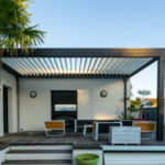 Trendy outdoor patio pergola. garden lounge, chairs, metal grill surrounded by landscaping