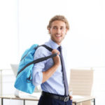 Young handsome businessman holding fitness bag in office. Gym after work
