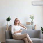 Aged woman sitting on couch holding remote control uses airconditioner